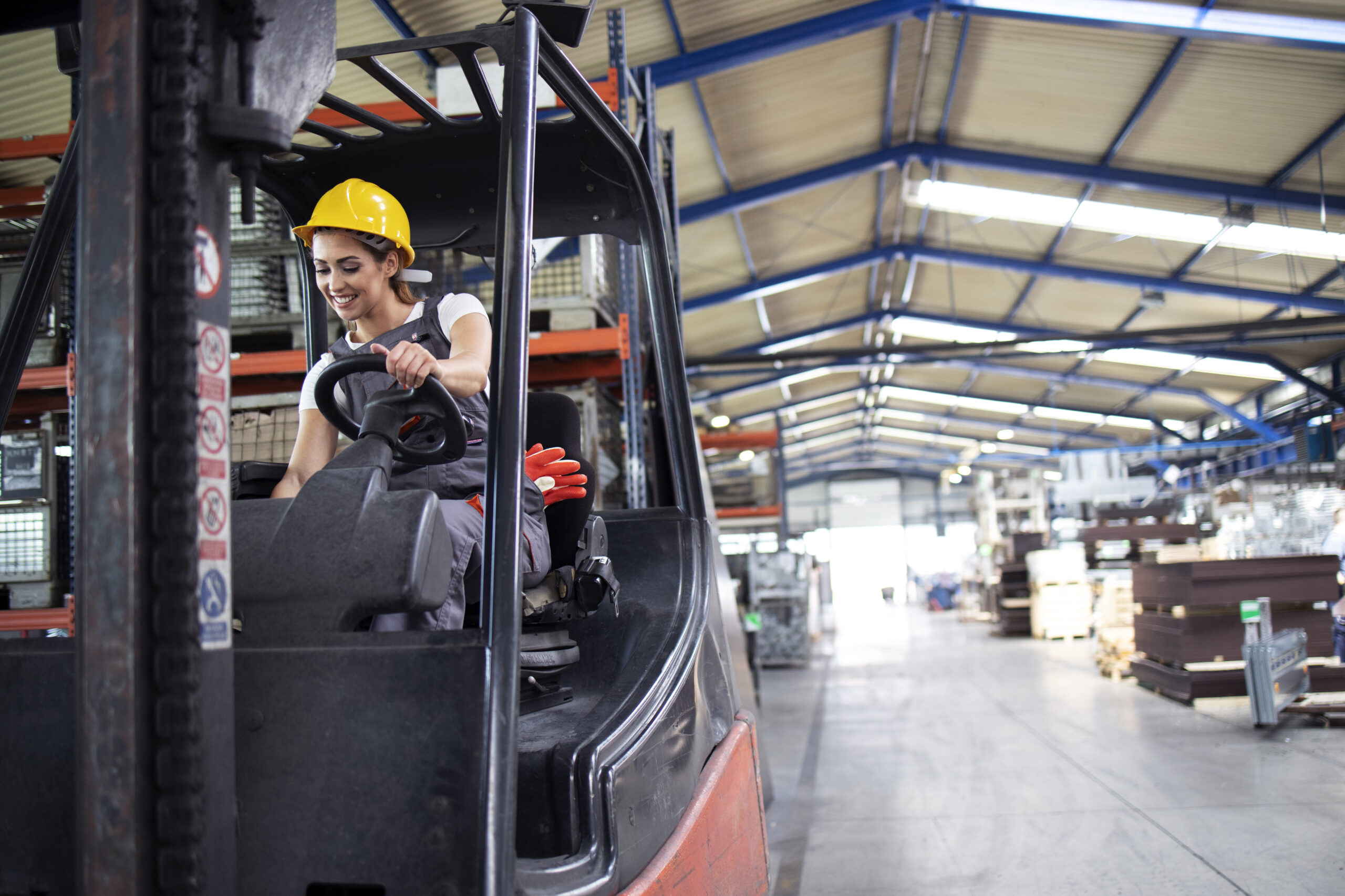 Professional female industrial driver operating forklift machine in factory's warehouse.